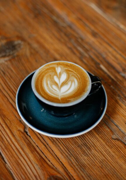 A beautifully crafted latte with intricate art in a blue cup on a wooden table.